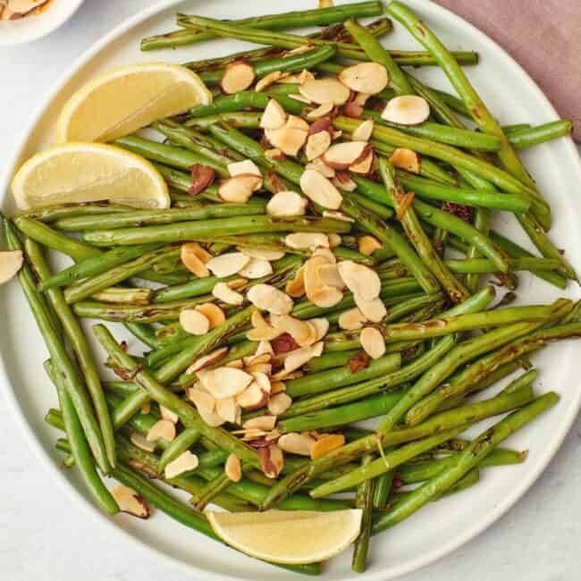 Close up of green beans with almonds with lemon wedges.