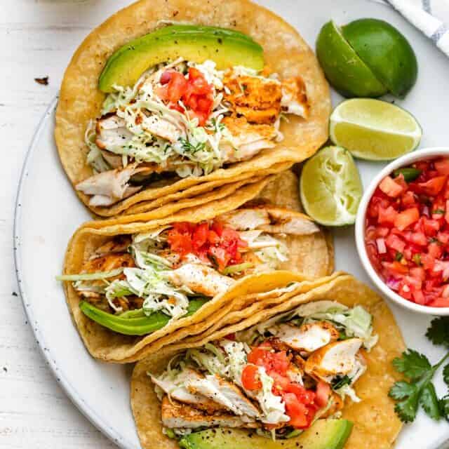 Large plate of grilled fish tacos topped with coleslaw, avocado and pico de gallo