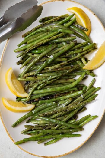 Large platter of grilled greens beans garnished with fresh lemon wedges.