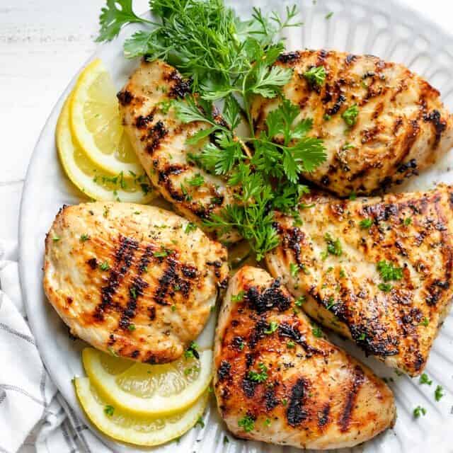 Grilled Lemon Chicken breasts on a plate with lemons and parsley