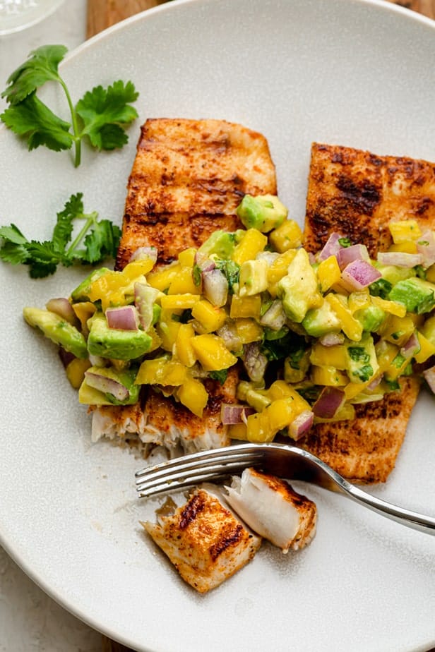 Cutting off mahi mahi fillet with mango avocado salsa on top