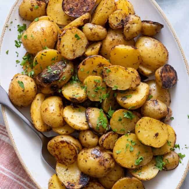 Platter with grilled potatoes garnished with parsley and spoon on side.