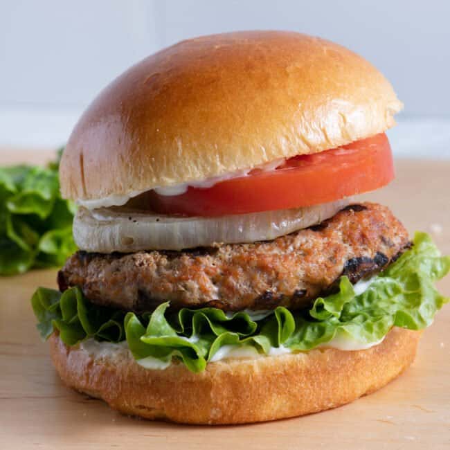 Assembled grilled turkey burger with lettuce, tomato, onion, and mayo.