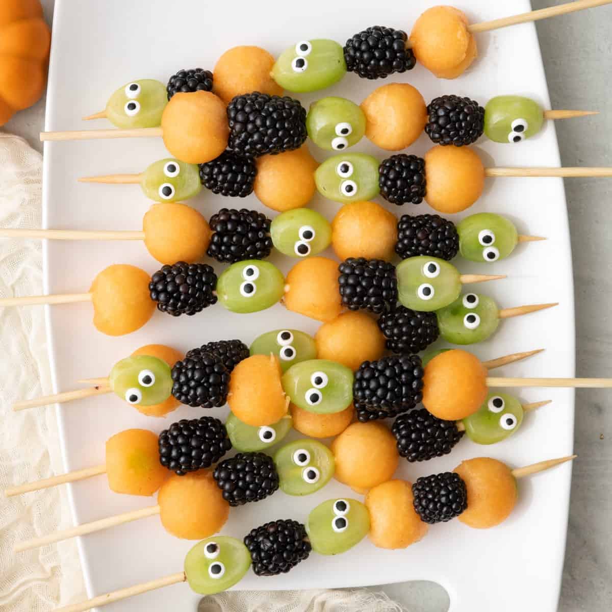 Halloween fruit kabobs on a platter, made with grapes, blackberries, and cantaloup.