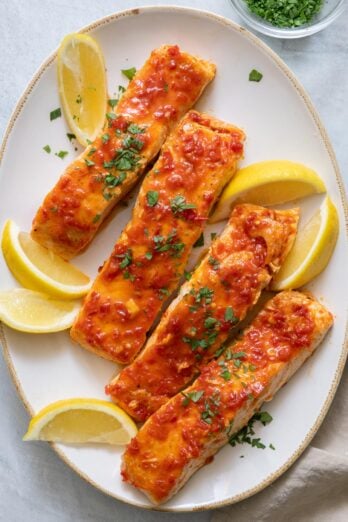 Large oval serving dish with 4 harissa glazed salmons filets garnished with lemon wedges and parsley.