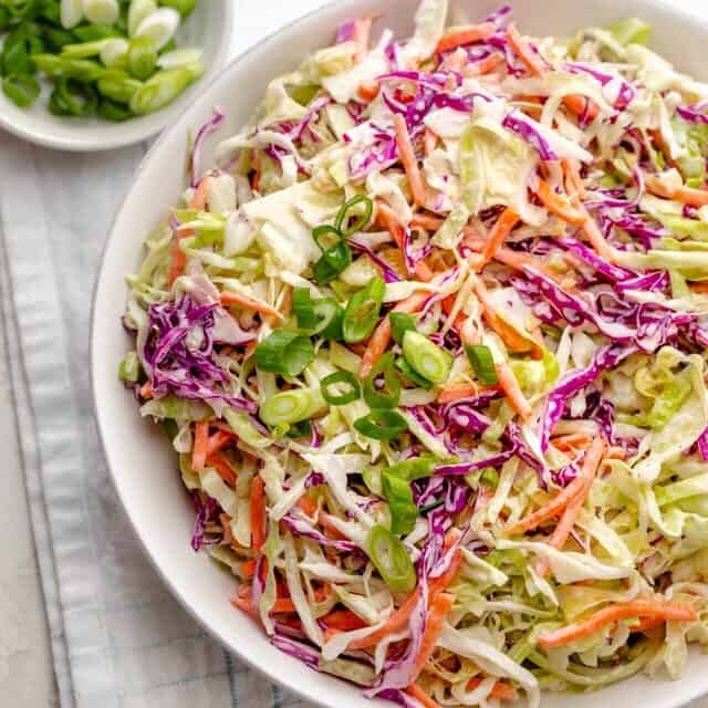 Healthy Coleslaw in a large bowl on a white napkin with green onions on the side