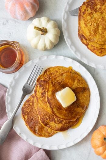 Final plating of recipe on a round white plate with butter and syrup on top, a fork to the side, and small pumpkin decoration around.