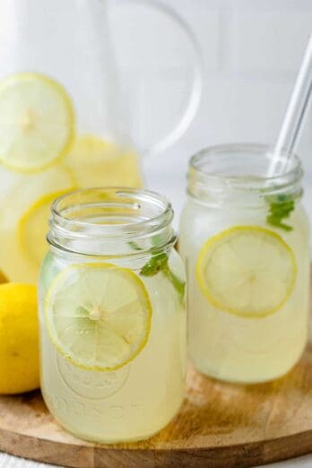 Homemade lemonade in a cup with glass jug in the background and lemons on the side