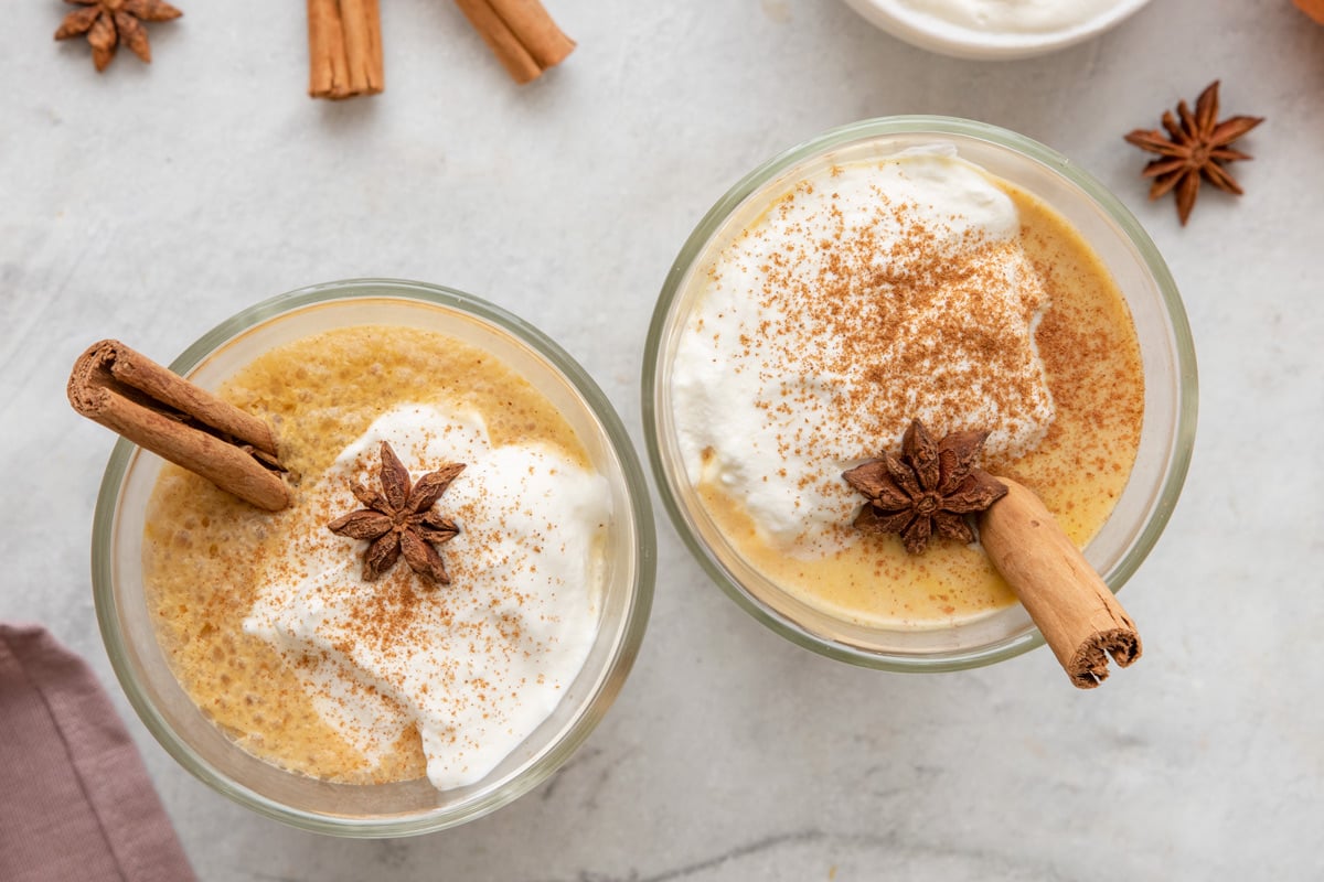 Overhead shot of 2 glasses of pumpkin spice latte topped with whipped cream, cinnamon stick inside, and a star anise in each.