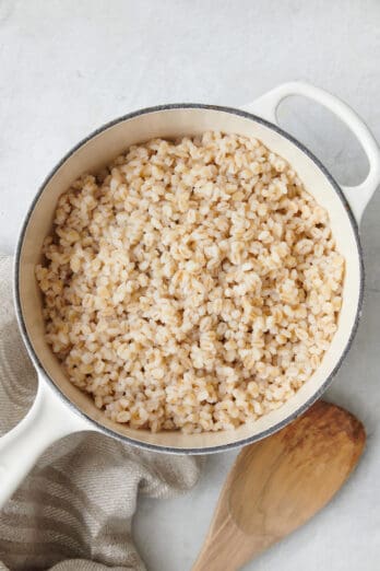 Cooked barley in a pot after fluffing with a wooden spoon nearby.