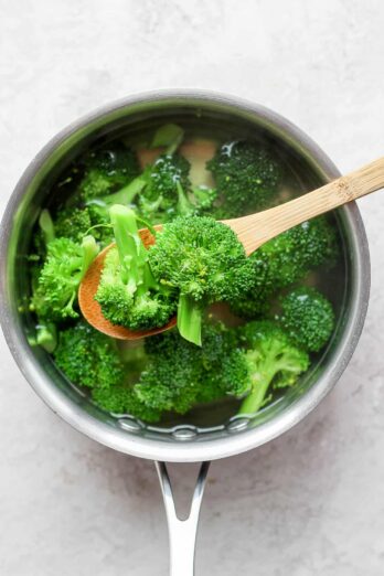 Cooked broccoli on slotted wooden spoon over pot of broccoli cooking