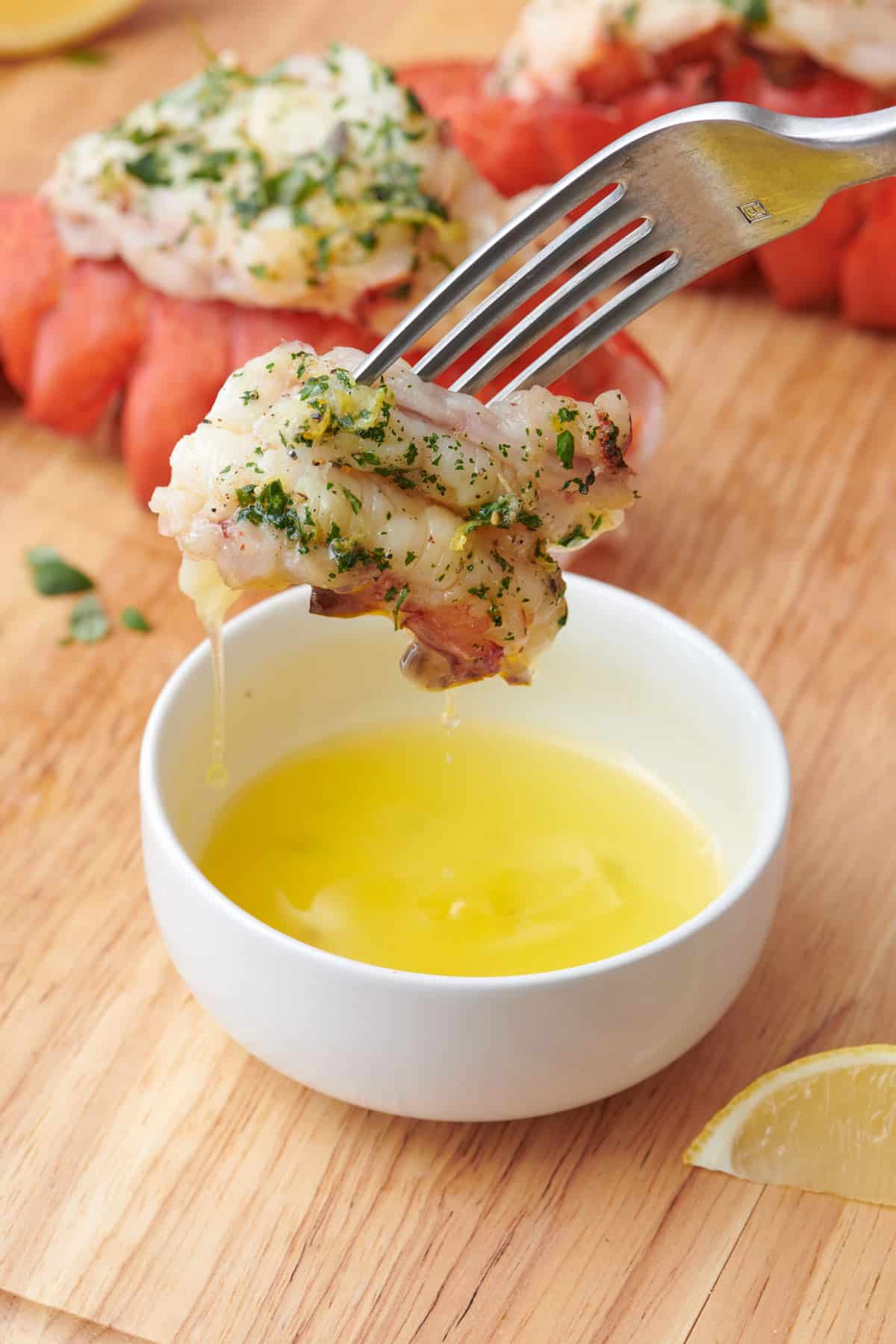 Fork lifting up a bite of lobster after dipping in melted butter.