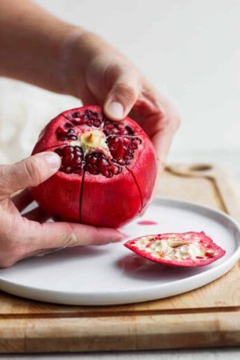 Large pomegranate with top sliced off and hands pulling at the segments