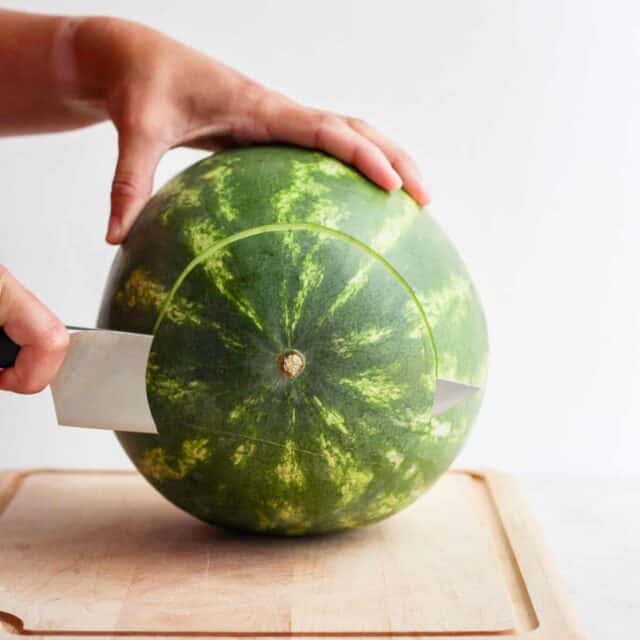 Large watermelon on cutting board with bottom part getting cut off