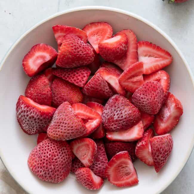 White bowl full of frozen halved strawberries.