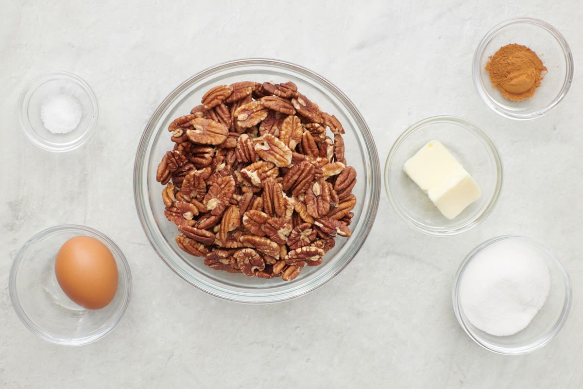 Ingredients for recipe in individual bowls: slat, egg, pecan halves, butter, cinnamon, and sugar.