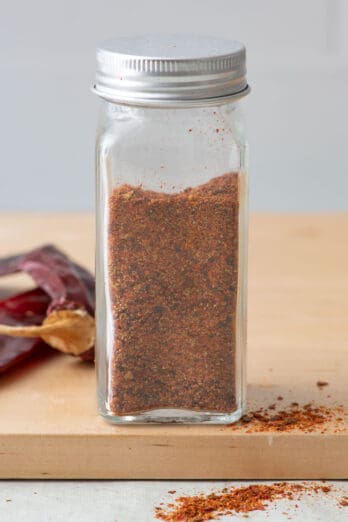 Homemade chili powder in a spice jar with dried chilis nearby.