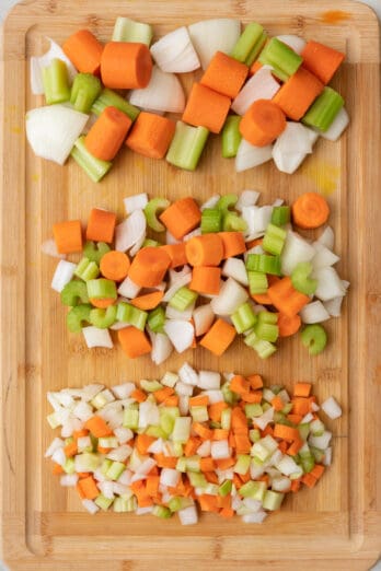 Three different sized blends of carrots, onions, and celery for a mirepoix lined up on a cutting board in rows.