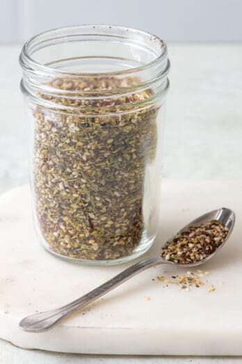 Homemade Za'atar seasoning in a spice jar with a spoonful of spice next to it.