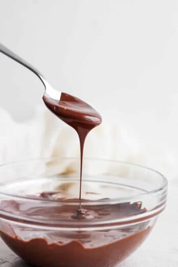 Melted chocolate in a clear glass bowl with spoon dripping