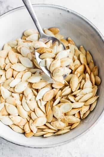 Small bowl of roasted pumpkin seeds with spoon scooping some.