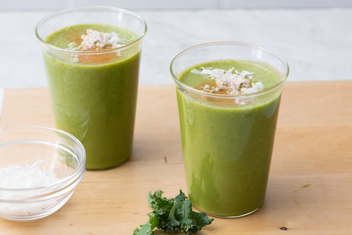 2 glasses filled with coconut kale smoothie, garnished with cinnamon and shredded coconut.