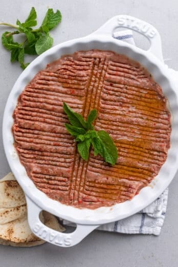 Round ceramic dish with Kebbeh Nayyeh pressed inside with decorative groves pressed into the raw beef mixture.