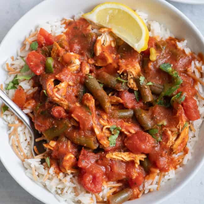 bowl of green bean stew served over Lebanese rice with lemon wedge