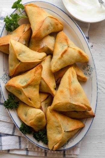 Large platter of spinach pies with small bowl of yogurt for dipping