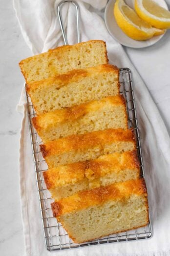 Lemon bread recipe sliced on a cooling rack with lemon wedges near by