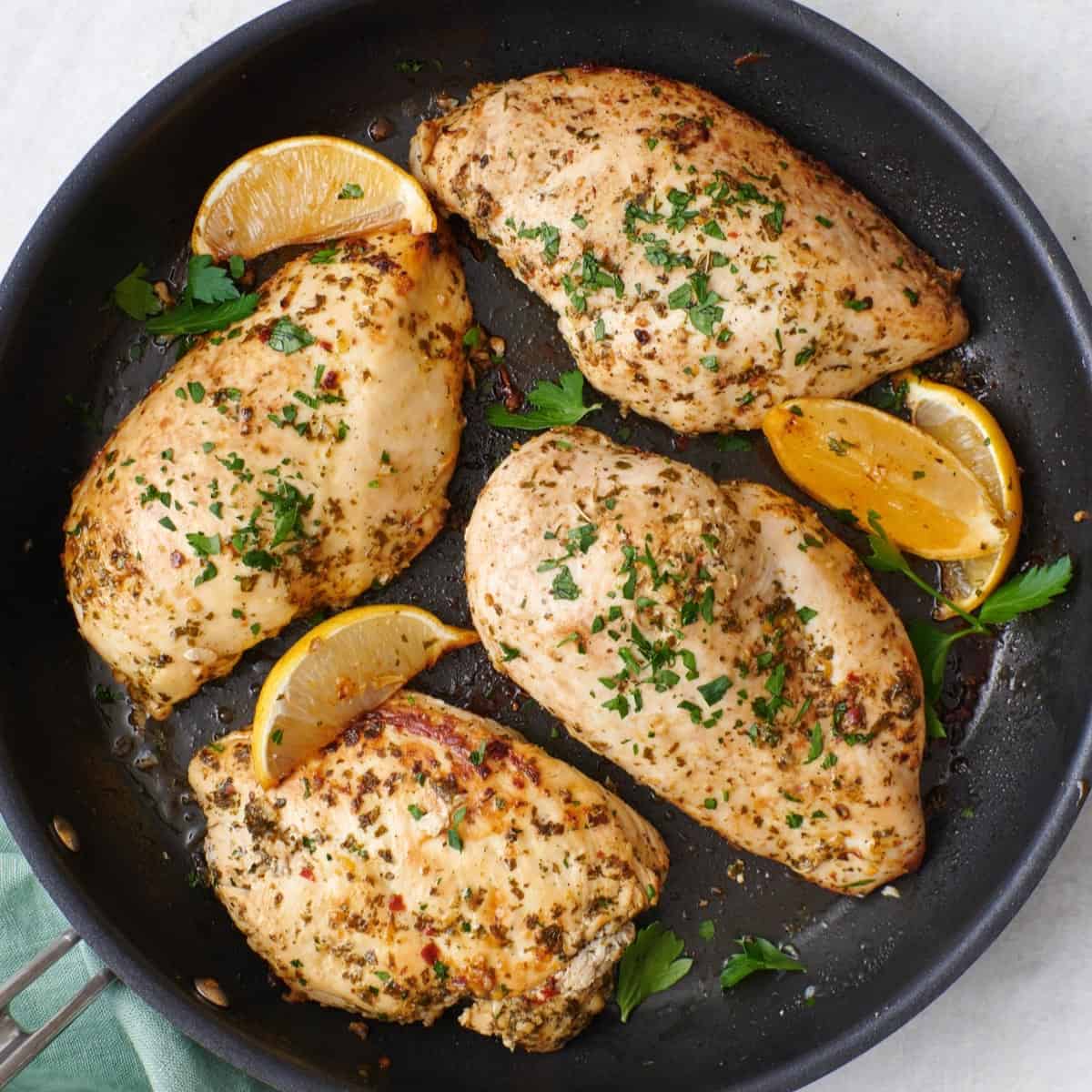 Lemon garlic chicken breasts in a skillet with lemon wedges.