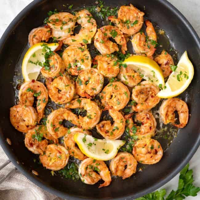 Shrimp in pan with lemon zest and squeezed lemon wedge, garnished with chopped fresh parsley.