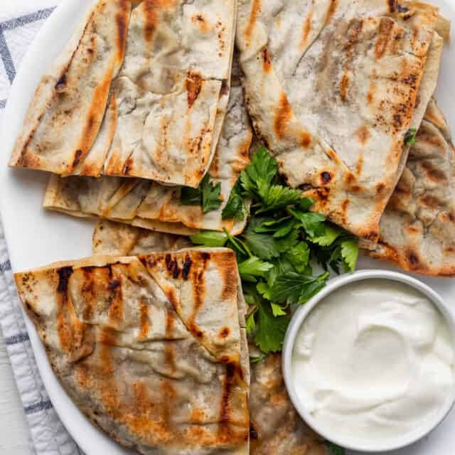 Lebanese meat stuffed pita triangles served on a white platter with a small bowl of yogurt and parsley for garnish