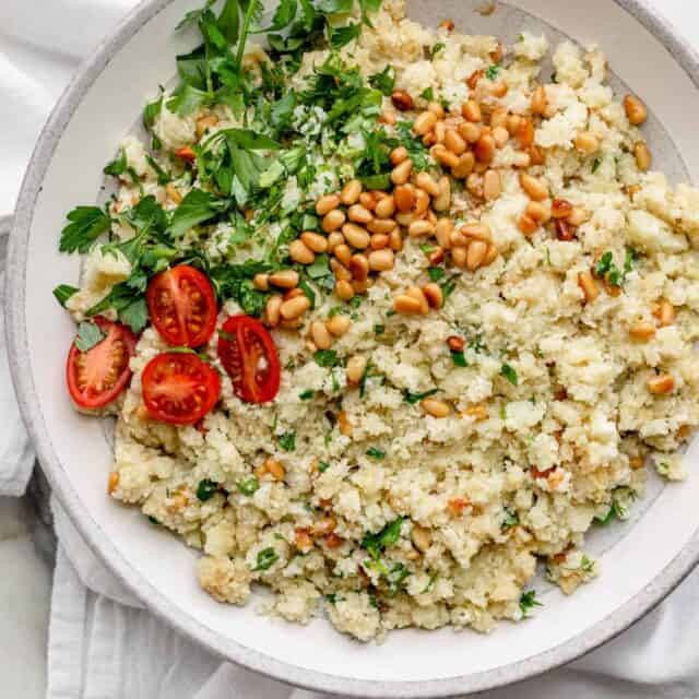 Mediterranean cauliflower rice in a large bowl with parsley and pinenuts