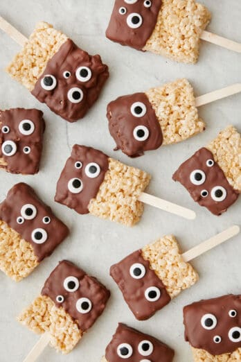 Monster rice krispie treats dipped in chocolate with googly eyes and on a stick.