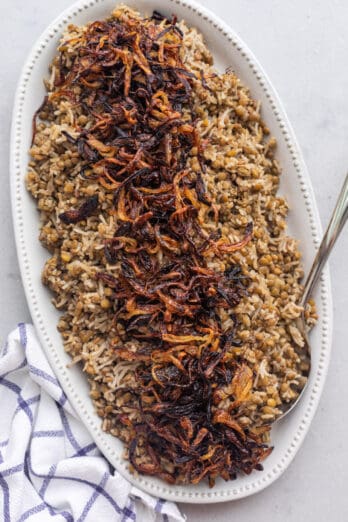 Large oblong decorative platter with Mujadara topped with crispy fried onions and a spoon dipped in.