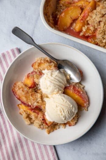 Peach crisp in a bowl served with two scoops of vanilla ice cream