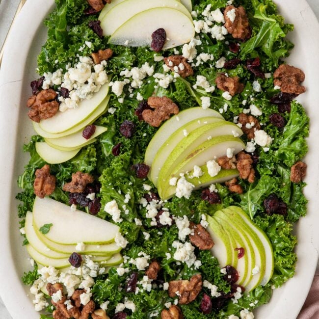 Final plating of the pear salad with dressed kale, pear, candied walnuts, dried cranberries, and cleu cheese.