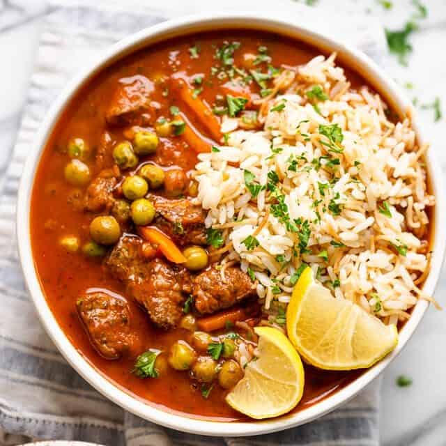 A bowl of peas and carrots stew garnished with lemon wedges