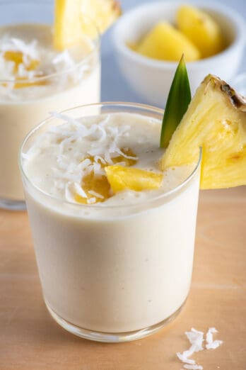 Two small cups of pina colada smoothies with pineapples on on the cup