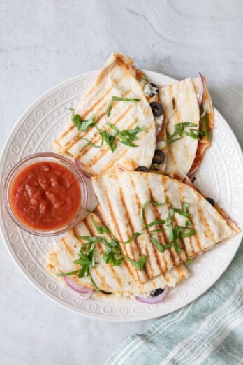 Recipe cut into hand held sizes on a round white plate with a side of marinara sauce for dipping.