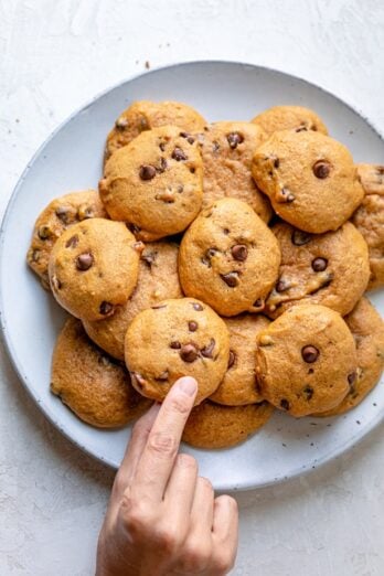 Hand grabbing a cookie from a plate full of pumpkin chocolate chips cookies