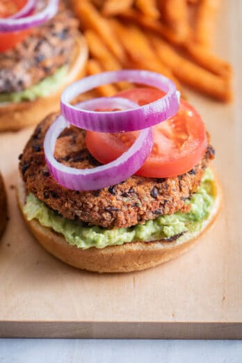 One quinoa burger topped with tomatoes and onions with sweet potato fries in background