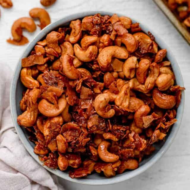 Large bowl of roasted cashews with coconut on white background