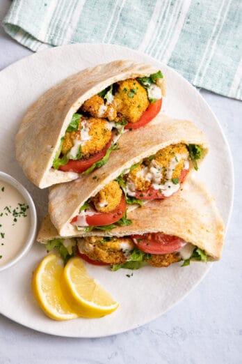 Plate of three pitas stuffed with roasted cauliflower served with lemon wedges.