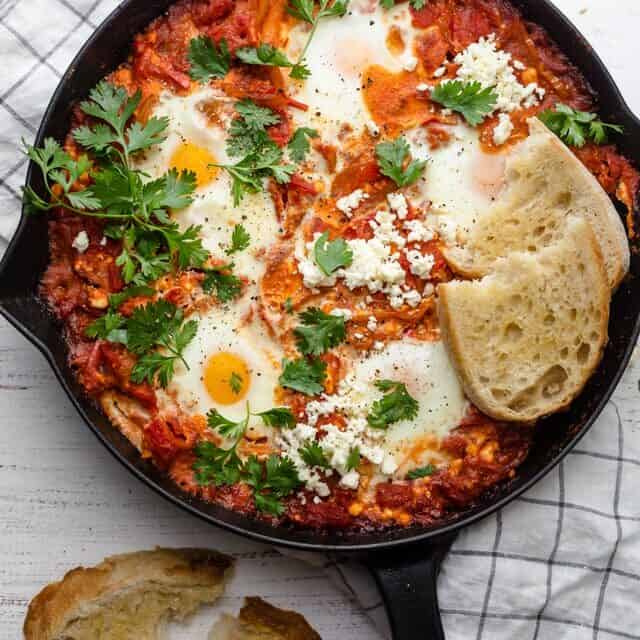 Shakshuka with Feta served with bread and cilantro in a cast iron skillet