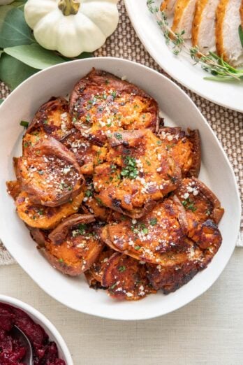 Sweet potato rounds garnished with parsley and parmesan in a serving dish with turkey slices and cranberry sauce nearby.