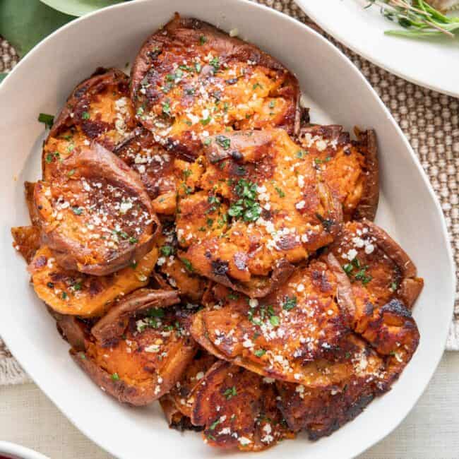 Sweet potato rounds garnished with parsley and parmesan in a serving dish with turkey slices and cranberry sauce nearby.