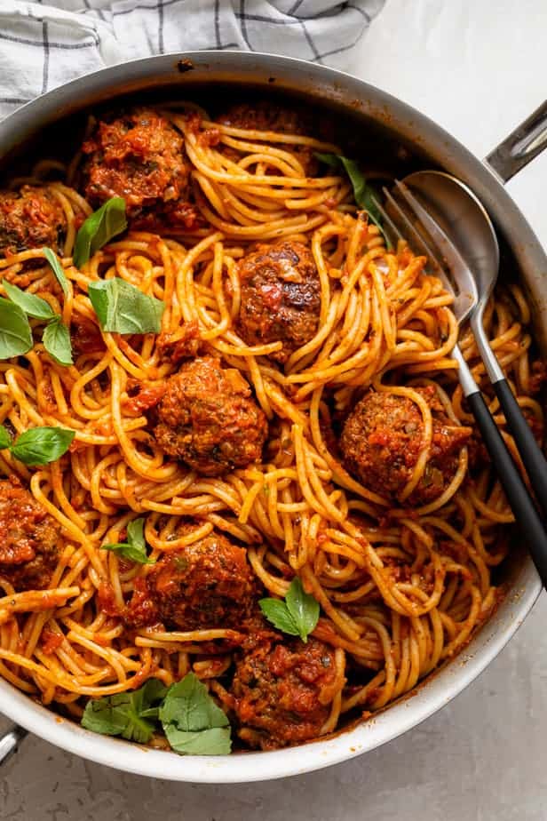 Large skillet of spaghetti and meatballs topped with basil