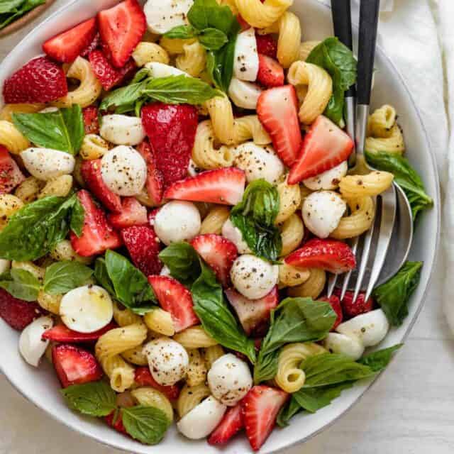 Strawberry caprese salad in large bowl with serving utensils in bowl